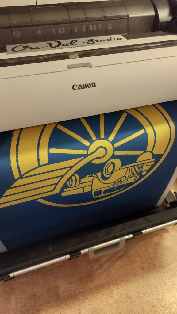 Canon-suurkuvatulostin tulostaa sinistä banneria, jossa kultainen tunnusmerkki, Ou-Vel Studio