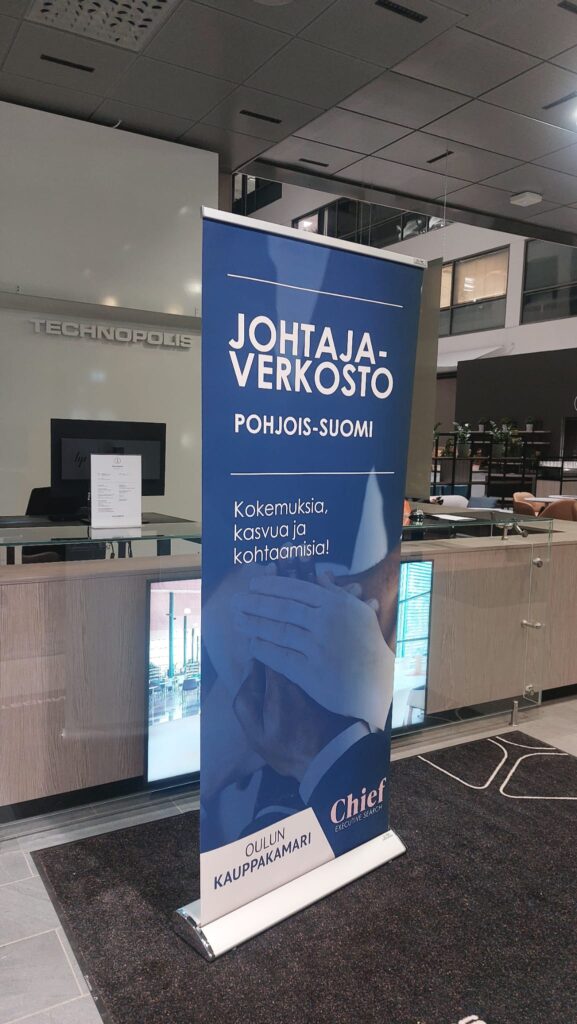 Sininen roll up -mainosteline aulassa, teksti Johtaja-verkosto Pohjois-Suomi