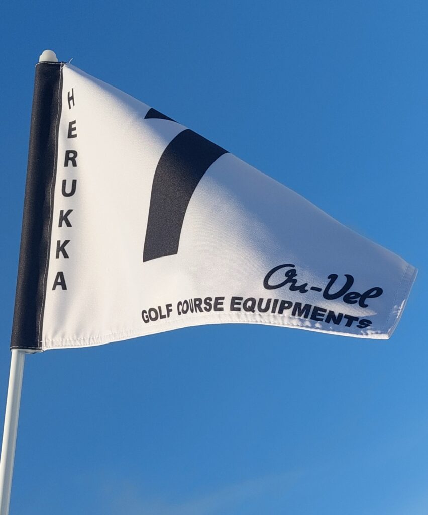 Valkoinen golflippu, jossa teksti Herukka ja Ou-Vel Golf Course Equipments, sinistä taivasta vasten